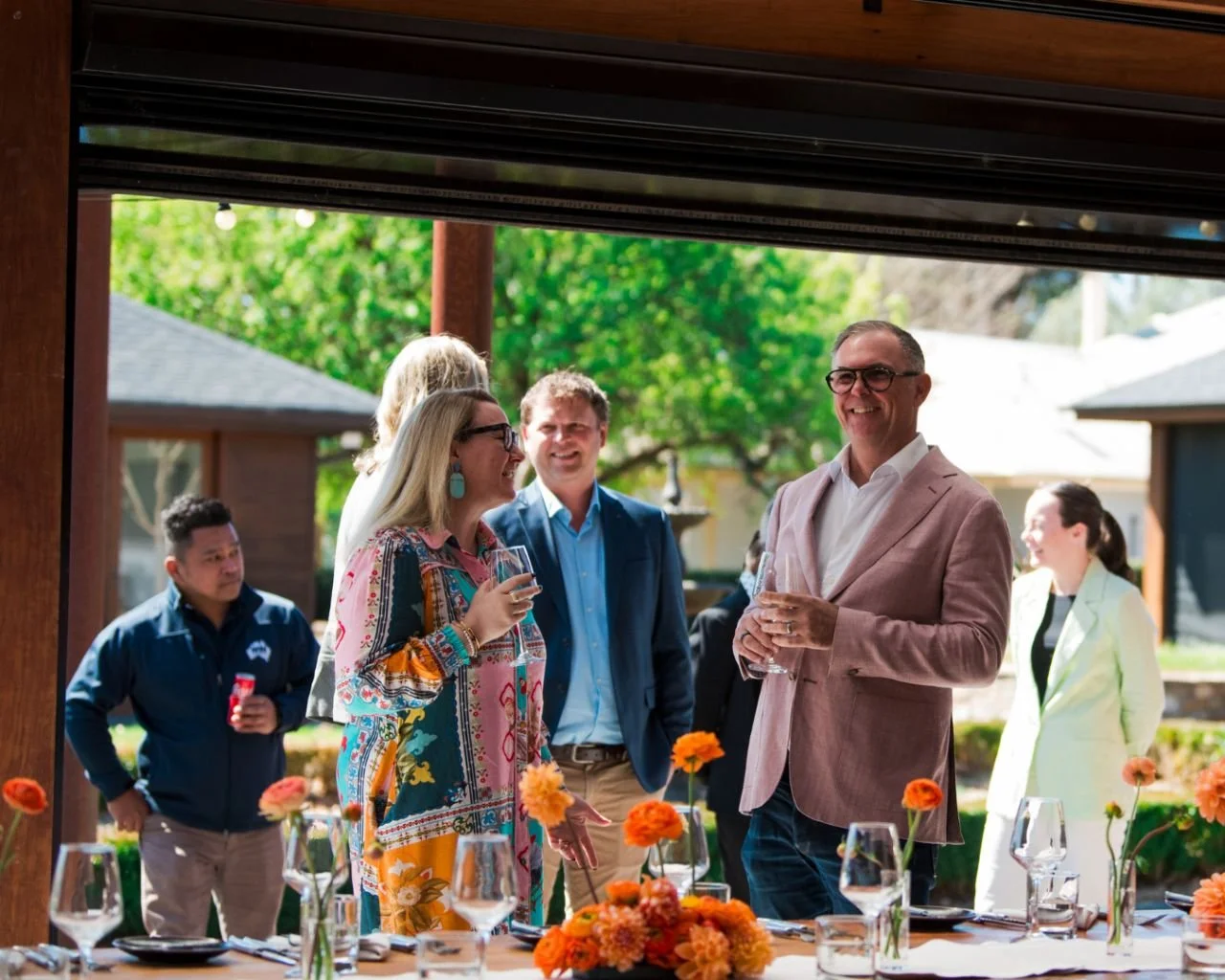 Family and friends gathering around a flower-filled dining table at Pialligo Estate